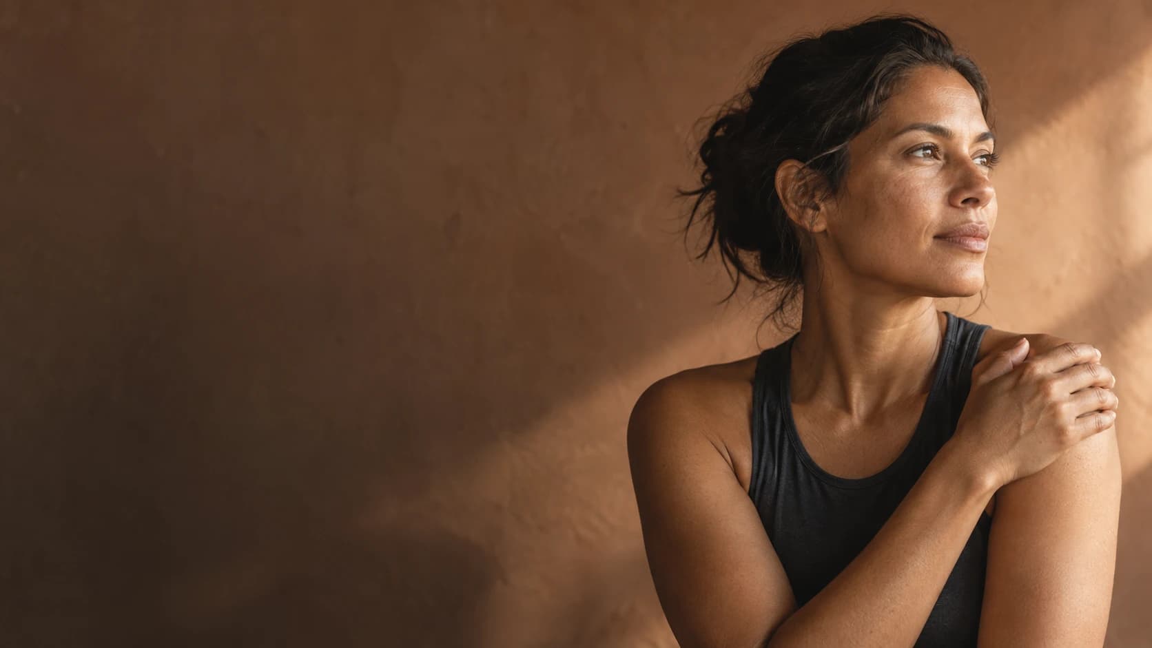 A woman in natural side light resting her hand on her shoulder